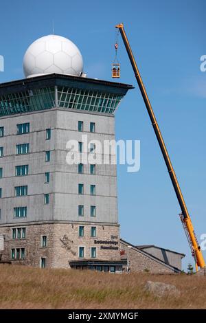 Schierke, Germania. 30 luglio 2024. Una gru del peso di diverse tonnellate si trova accanto alla torre Brocken. Sul tetto del Brockenherberge sono attualmente in fase di installazione nuove listelli per tetto. Poiché i lavori si svolgono ad altezze elevate nell'area del radar di volo, il sistema radar di volo sul Brocken è stato spento per diverse settimane. Crediti: Matthias Bein/dpa/Alamy Live News Foto Stock