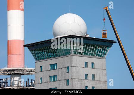 Schierke, Germania. 30 luglio 2024. Una gru del peso di diverse tonnellate si trova accanto alla torre Brocken. Sul tetto del Brockenherberge sono attualmente in fase di installazione nuove listelli per tetto. Poiché i lavori si svolgono ad altezze elevate nell'area del radar di volo, il sistema radar di volo sul Brocken è stato spento per diverse settimane. Crediti: Matthias Bein/dpa/Alamy Live News Foto Stock