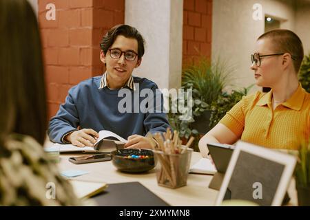 Giovane uomo birazziale che indossa occhiali da vista che racconta i risultati del sondaggio durante l'incontro con il team di marketing in un ufficio moderno Foto Stock