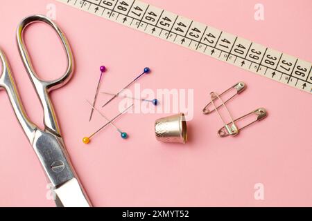 Forbici, perni da cucire, ditale e accessori per cucire su sfondo rosa Foto Stock