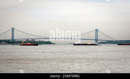 New York, USA - 7 giugno 2019: Le navi cargo navigano sotto il ponte Verrazzano-Narrows in condizioni meteorologiche miti. Foto Stock
