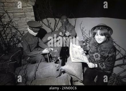 1985, una giovane visitatrice che fa scattare la sua foto seduta in sacchi di sabbia che reggono un giornale e indossano un casco di latta, noto come casco di Brodie all'interno di una mostra che presenta un modello di trincea WW1 sul fronte occidentale con solidi fittizi, uno con maschera a gas, che sparano con una mitragliatrice, Foto Stock