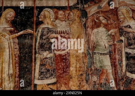 Uomo dai capelli rossi con corna e donna elegante con lunghi piedistalli dorati con santi. Uno dei numerosi affreschi tardo medioevali della Basilica-Duomo di San Vigilio a Trento, in Italia, che raffigurano scene della leggenda di San Giuliano (San Giuliano Ospitaliero). Foto Stock