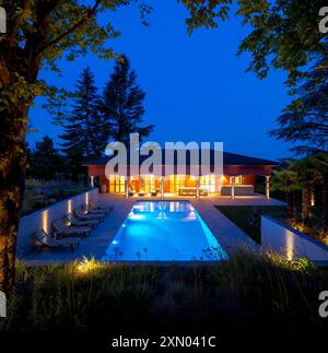 Casa con una splendida piscina davanti, fotografie serali o notturne. Ci sono molte sedie a sdraio a sinistra. Cielo blu scuro, tutto in mezzo alla natura. Foto Stock