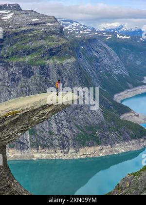 Un avventuriero solitario si erge precariamente su una sporgenza di roccia naturale, affacciato sulle acque mozzafiato dei fiordi e sulle aspre montagne della Norvegia. Trolltunga, Norvegia Foto Stock