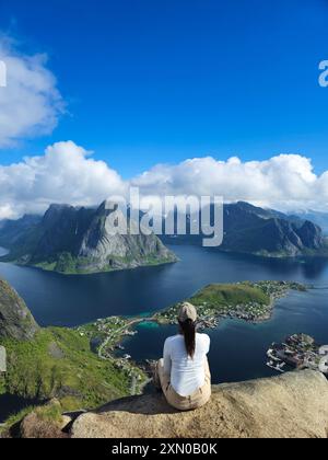 Una figura solitaria si rilassa su un affioramento roccioso, ammirando le viste panoramiche mozzafiato delle lussureggianti montagne e delle tranquille acque delle splendide isole Lofoten della Norvegia. Foto Stock