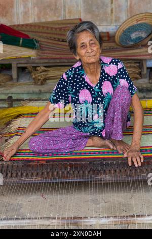 Anziana donna vietnamita che tesseva materassini da canne essiccate e tinte su telaio nel villaggio di tra Nhieu, Quảng Nam, Vietnam centrale, Asia a giugno Foto Stock