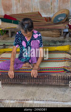 Anziana donna vietnamita che tesseva materassini da canne essiccate e tinte su telaio nel villaggio di tra Nhieu, Quảng Nam, Vietnam centrale, Asia a giugno Foto Stock