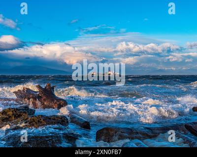 Onde che si infrangono sulla riva dell'isola di Gabriola, con il faro sull'Isola d'ingresso visibile in lontananza Foto Stock