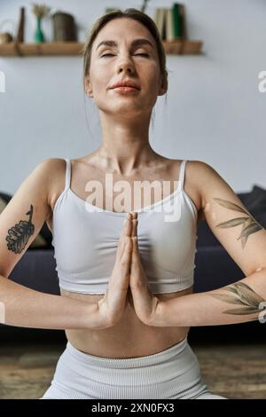 Una giovane donna in abbigliamento sportivo siede in un appartamento moderno, praticando yoga con gli occhi chiusi, concentrandosi sulla meditazione e il benessere mentale. Foto Stock