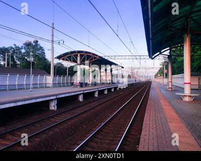 Mosca, Russia, giugno 2019: Veduta della piattaforma di una piccola stazione suburbana, splendidamente illuminata dal sole che tramonta. Binari del treno, gente che aspetta Foto Stock