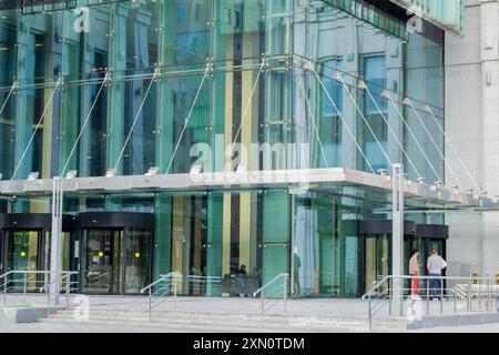 Ingresso in vetro ad un moderno edificio di uffici con persone all'interno e vicino ad esso. Foto Stock