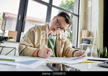 Un giovane con la sindrome di Down si siede a una scrivania e lavora su documenti. Foto Stock