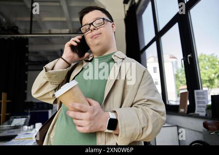 Un giovane con la sindrome di Down tiene una tazza di caffè mentre parla al telefono. Foto Stock