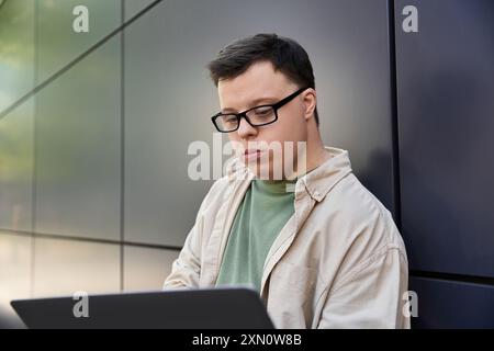 Un uomo con la sindrome di Down si siede fuori, a lavorare sul suo portatile. Foto Stock