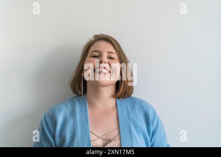 Giovane donna allegra e di grandi dimensioni con ampio sorriso in piedi su sfondo bianco e semplice. Foto Stock