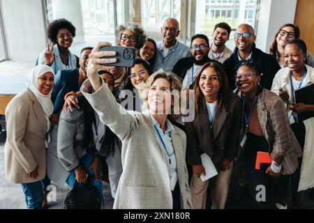 Un gruppo di colleghi allegri che scattano un selfie insieme a un evento aziendale, sottolineando il lavoro di squadra e il cameratismo. Foto Stock