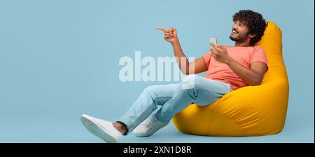 Uomo indiano felice con smartphone che punta allo spazio di copia Foto Stock