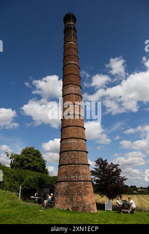 Camino alto in mattoni a Crofton Beam Engines in mezzo a un panoramico campo verde con gente che si rilassa e si gode la giornata di sole sotto un cielo blu con nuvole. Foto Stock