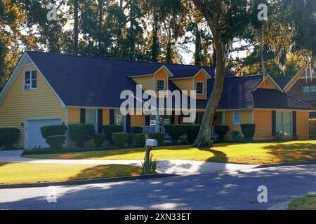 Un'affascinante casa gialla con un prato ben tenuto e grandi alberi che forniscono ombra Foto Stock