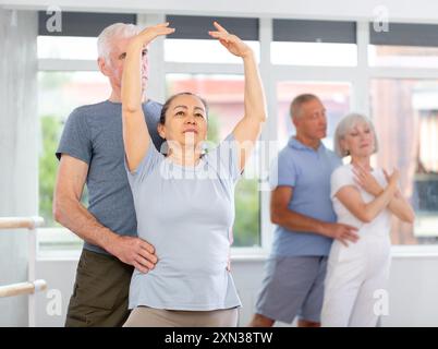 Coppia di ballerini maturi contemporanei che eseguono graziose coreografie, allenando il balletto entrechat in posa nella sala del balletto Foto Stock