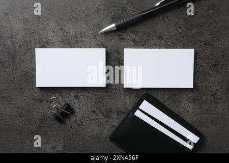 Porta carte di credito in pelle con biglietti da visita vuoti, penna e clip legante su tavolo testurizzato grigio, disposizione piatta. Mockup per il design Foto Stock