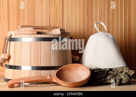 Frusta per sauna in quercia, cappello in lana di feltro, secchio e mestolo su una superficie in legno Foto Stock