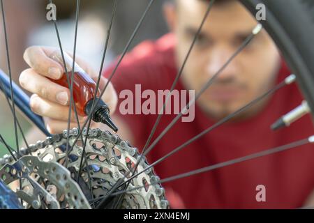 primo piano della mano maschile che mette l'olio sulla catena della bicicletta, lubrifica la catena della bicicletta, lubrifica una catena della bicicletta, manutenzione della bicicletta Foto Stock