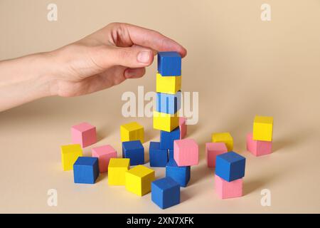 Donna che mette un cubo colorato ad altri su sfondo beige, primo piano Foto Stock