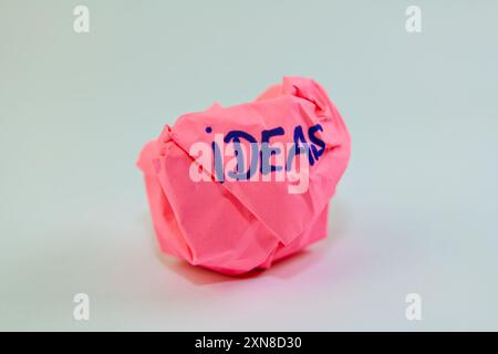 Una pallina di carta rosa scartata etichettata "idee", che rappresenta un blocco creativo o concetti rifiutati. Foto Stock