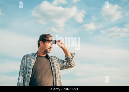 Ritratto di un agricoltore sul campo che indossa il cappello del camionista contro il cielo estivo, attenzione selettiva Foto Stock