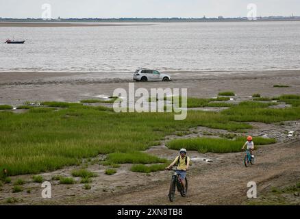 I ciclisti sul lungomare, accanto a un'auto che ha guidato fino alla spiaggia, e sono rimasti bloccati sulla sabbia, Lytham St Annes, Lancashire Regno Unito Foto Stock