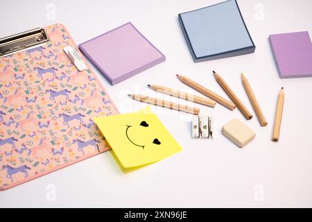 Un portadocumenti rosa con un adesivo sorridente e un mucchio di matite e penne Foto Stock