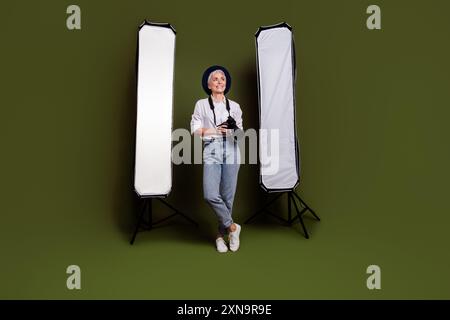 Foto a tutta lunghezza di un'incantevole camerawoman da sogno indossa camicia bianca cappello che registra video spazio vuoto sfondo di colore verde isolato Foto Stock