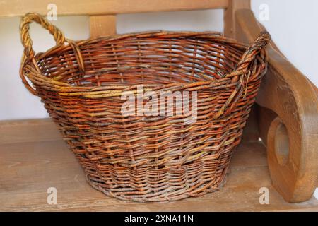 Cestino vintage in vimini su una panca di legno. Contenitore artigianale nella cucina del cottage. Vita di campagna. Foto Stock