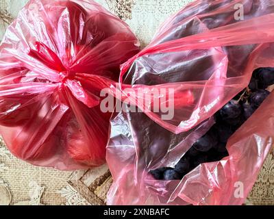 Primo piano di uva e pomodori freschi in sacchetti di plastica rosa su una superficie a motivi geometrici Foto Stock