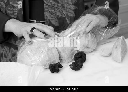 Primo piano di mani caucasiche che recuperano pane a lievitazione naturale da un sacchetto, preparandosi a preparare un panino gourmet con tartufi francesi con diamanti neri. Foto Stock