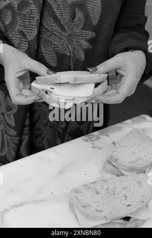 Primo piano di mani femminili caucasiche che tengono in mano un panino gourmet al tartufo francese con diamanti neri fatto con pane a lievitazione naturale e formaggio fuso. STATI UNITI Foto Stock