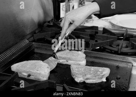 Primo piano di una donna caucasica che prepara un sandwich gourmet al tartufo francese con diamanti neri su una griglia, con pane a lievitazione naturale e formaggio fuso. STATI UNITI Foto Stock