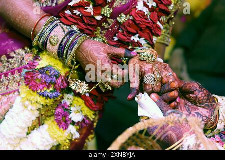 Le teneri mani di una sposa indiana ricoperte di tatuaggio all'henné tengono la mano dello sposo e la cerimonia dell'anello. Foto Stock