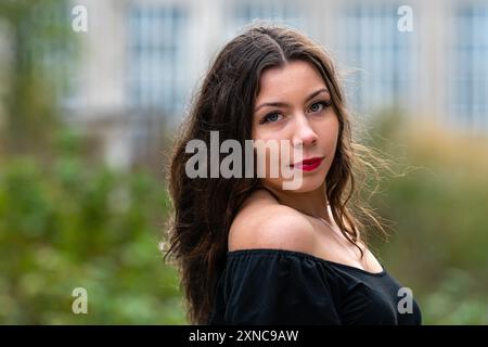 Una donna con i capelli lunghi e le labbra rosse posa con sicurezza in un'area all'aperto. Foto Stock