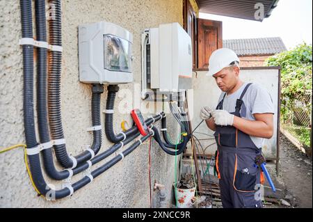 Elettricista che installa il sistema a pannelli solari. Tecnico in elmetto e guanti che fanno inverter di cablaggio elettrico e scatola elettrica. Concetto di energia alternativa e rinnovabile. Foto Stock