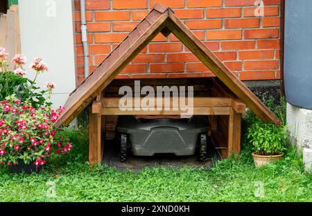 Rasaerba robot all'interno del garage di falciatrici in legno fatte in casa all'aperto in estate nel giardino di casa. Foto Stock