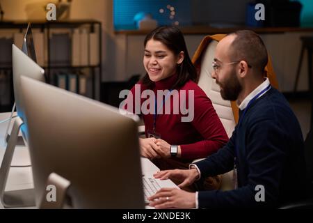 Ritratto ad alto angolo di due sviluppatori di software che collaborano al progetto e guardano con sorriso gli schermi dei computer Foto Stock