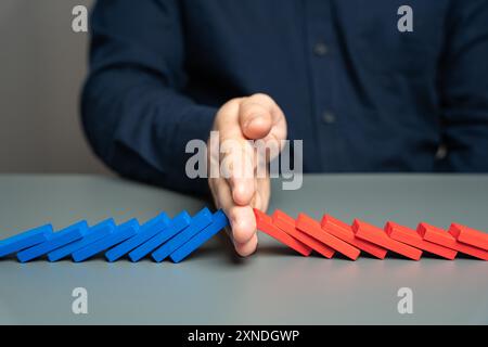 Un uomo impedisce a due catene di domino di scontrarsi. Il concetto di fermare un conflitto e prevenire un'ulteriore escalation. Elezioni e confronto della Foto Stock