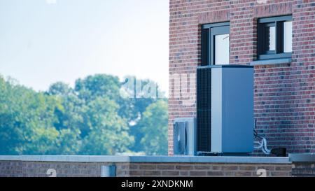 Una moderna pompa di calore per sorgenti d'aria poggia sul tetto di un edificio contemporaneo, circondato dal verde sotto un cielo azzurro. pompa di calore della fonte d'aria di traduzione in pompa di calore Foto Stock