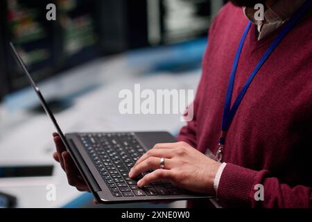 Vista laterale primo piano di un uomo irriconoscibile che tiene un laptop aperto in piedi all'interno DELL'ufficio IT e dell'ufficio di sicurezza informatica digitando a mano sullo spazio di copia della tastiera Foto Stock