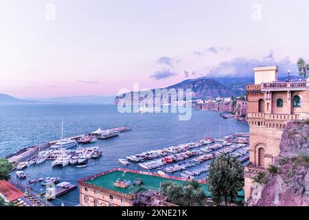 Affascinante vista serale del porto di Sorrento con yacht attraccati, scogliere panoramiche e un cielo pastello in Italia. Foto Stock