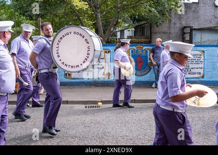 Ballyclare, Irlanda del Nord - 27 agosto 2022: Ballycraigy Sons of Ulster Flute Band passando il murale paramilitare UDA lealista. Foto Stock