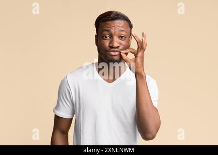 Afro uomo rendendo il labbro di Zip gesto Standing, Studio Shot Foto Stock